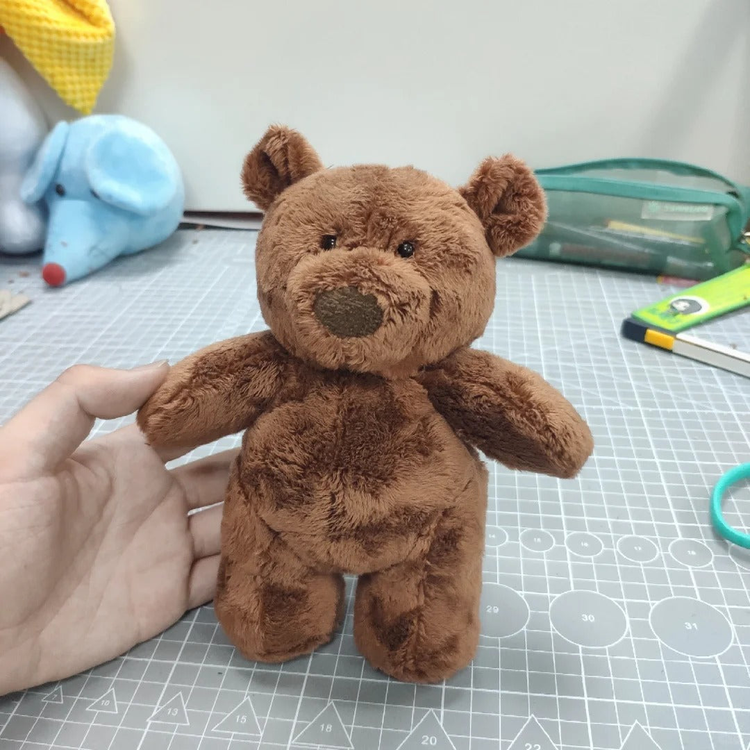 Brown teddy bear held by a hand on a cutting mat with tools in the background