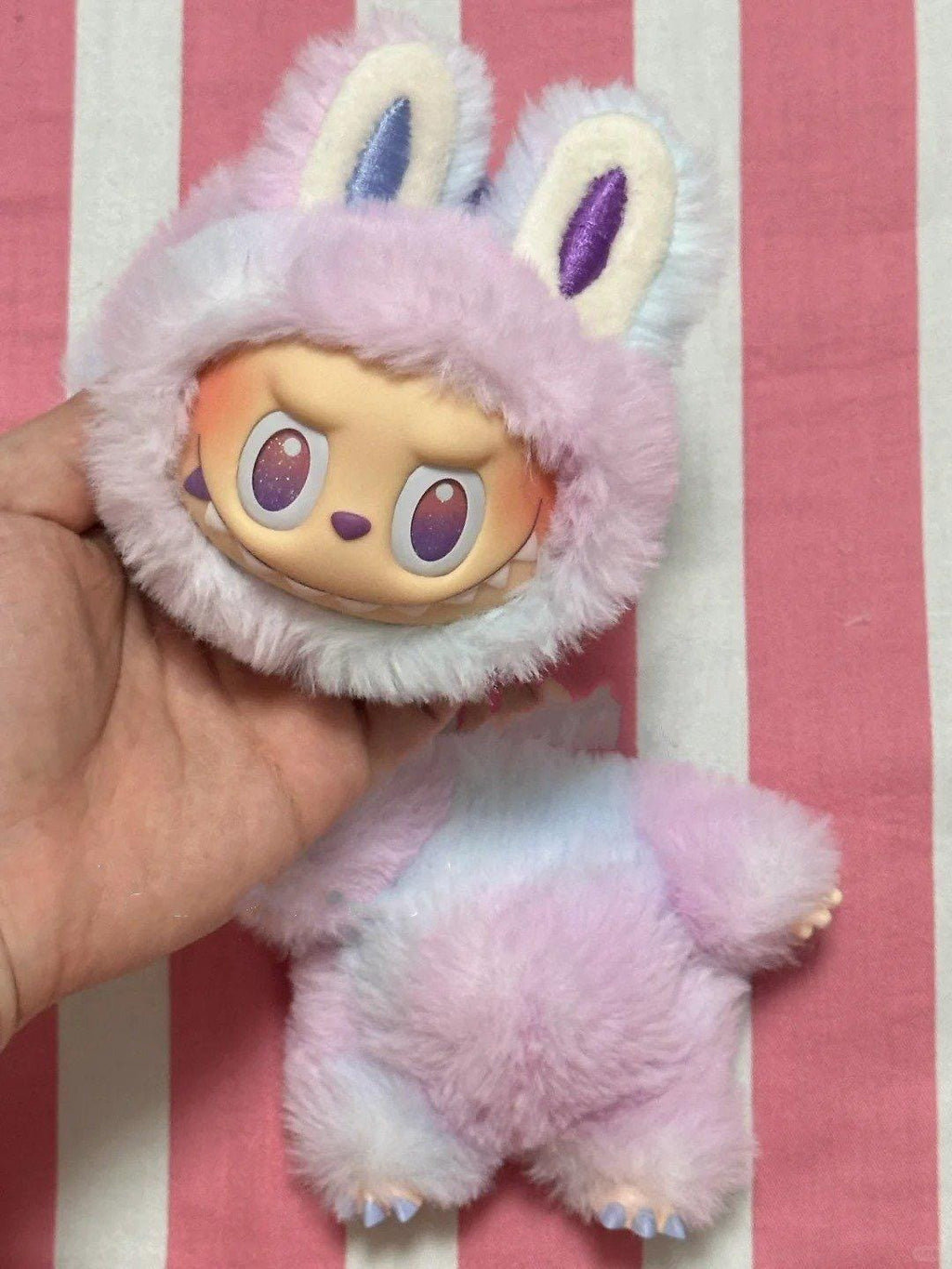 How to make a labubu? labubu Plush toy with a laububu face held against a striped pink and white background