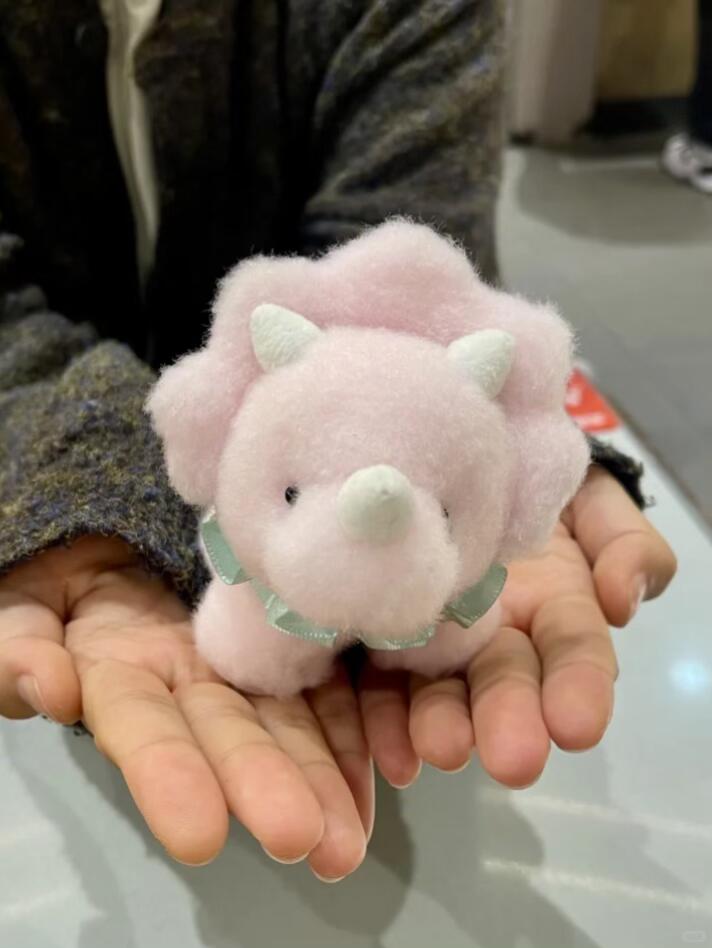 Pink dinosaur plush toy held in hands on a light background