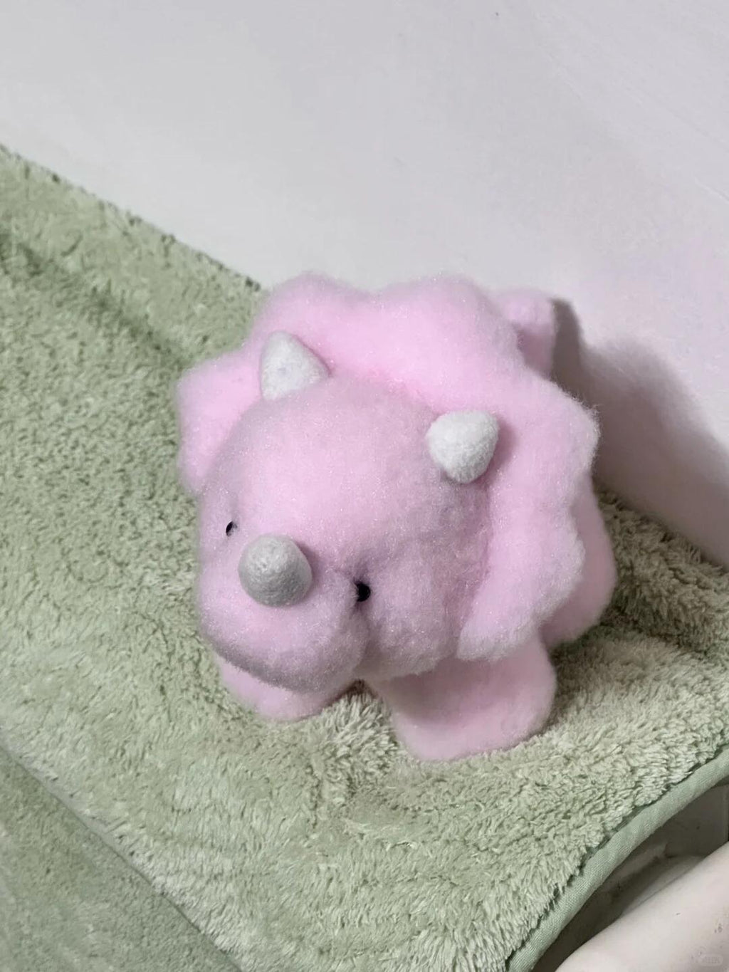 Pink plush dinosaur toy on a green towel