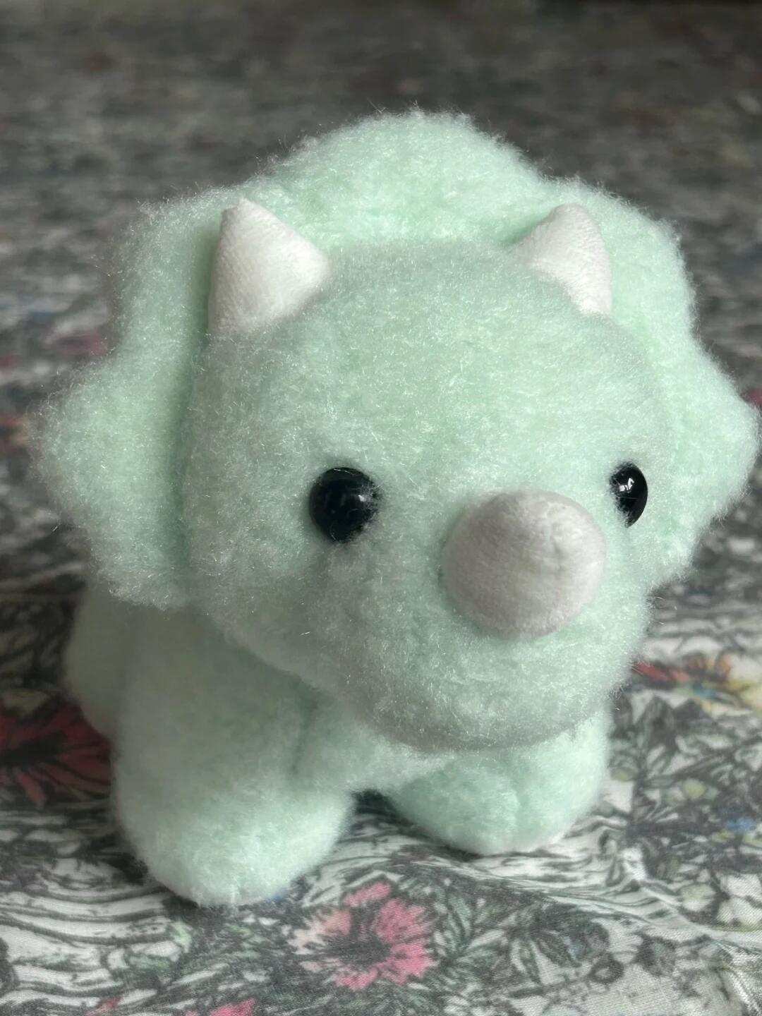 Light green dinosaur plush toy on a floral fabric background