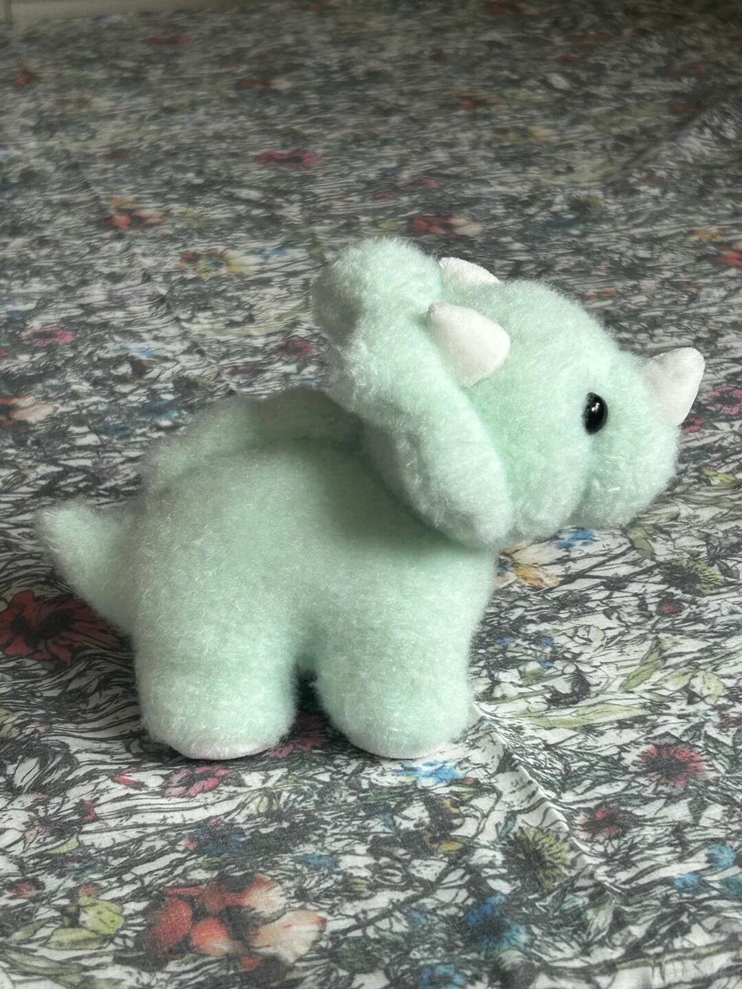 Small green stuffed dinosaur toy on a patterned fabric background
