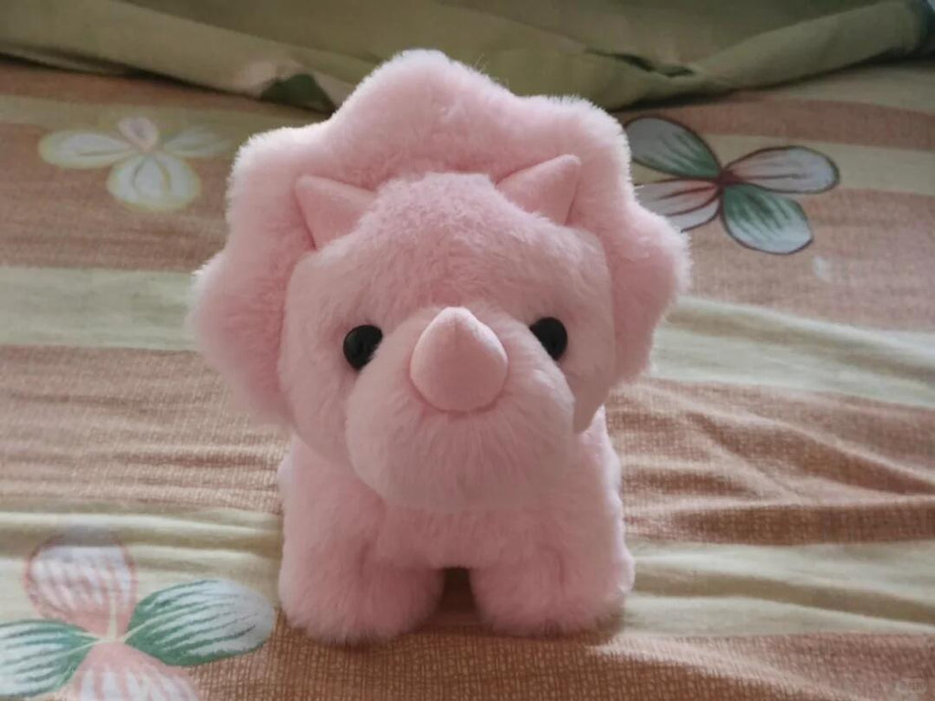 Pink dinosaur plush toy resembling a dinosaur on a patterned fabric background