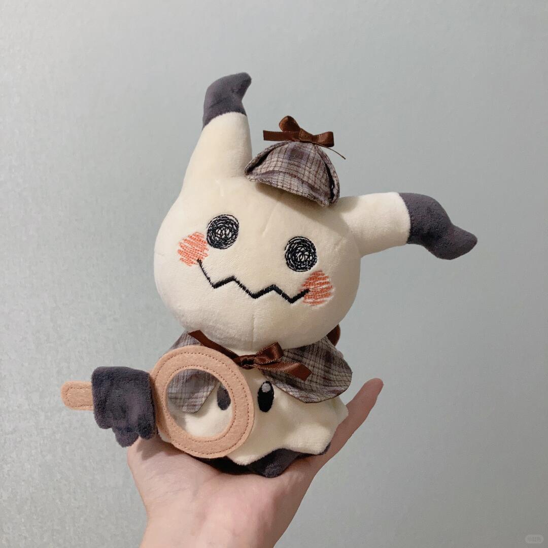 Mimikyu Plush toy resembling a detective cat held in a hand against a gray background