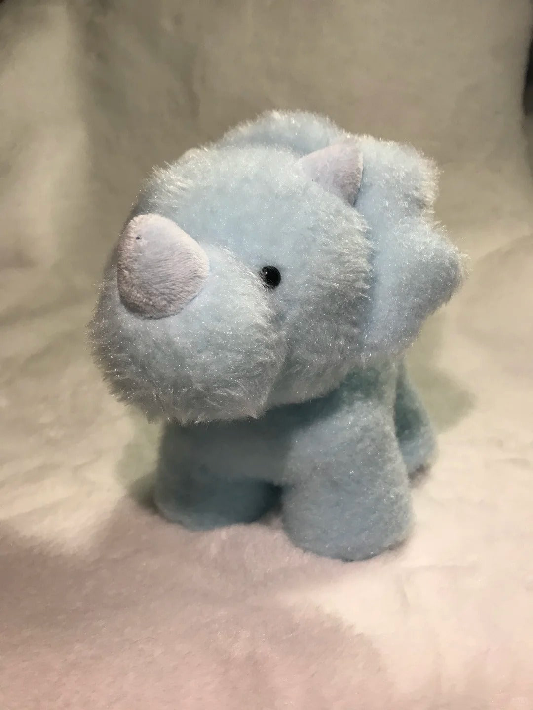 Blue dinosaur plush toy on a beige blanket