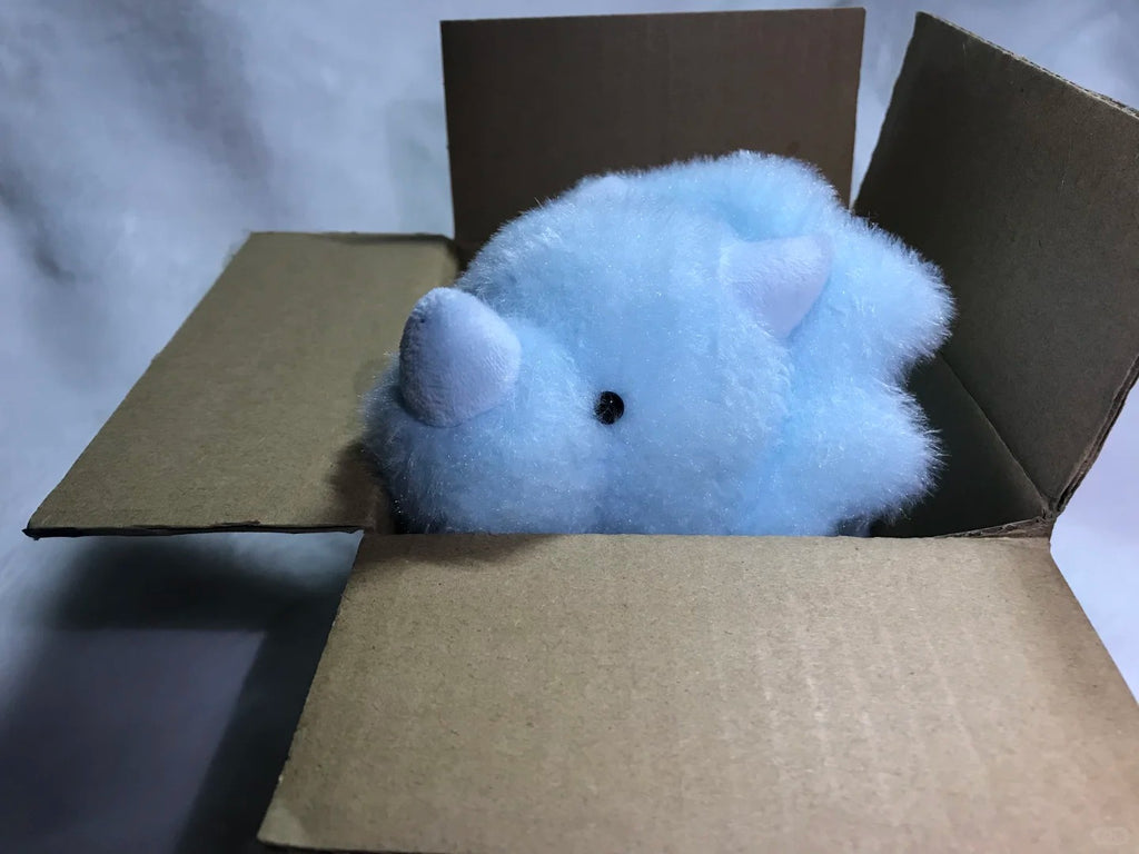 Blue dinosaur plush toy inside a cardboard box on a light gray background
