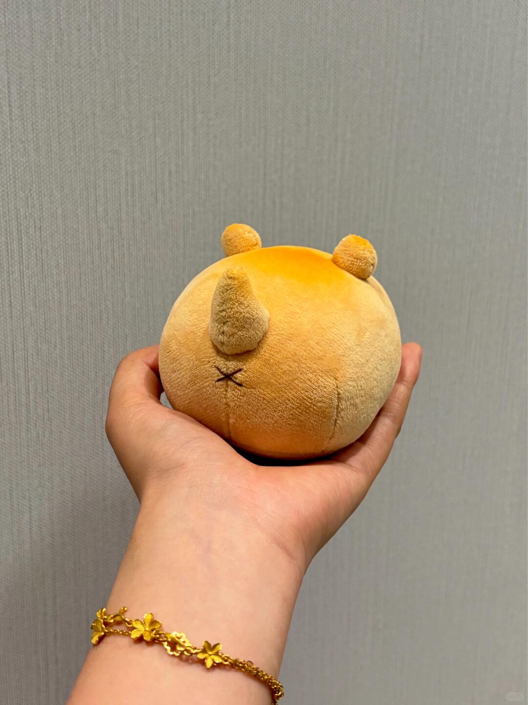 Hand holding a small round dog plush toy against a plain background