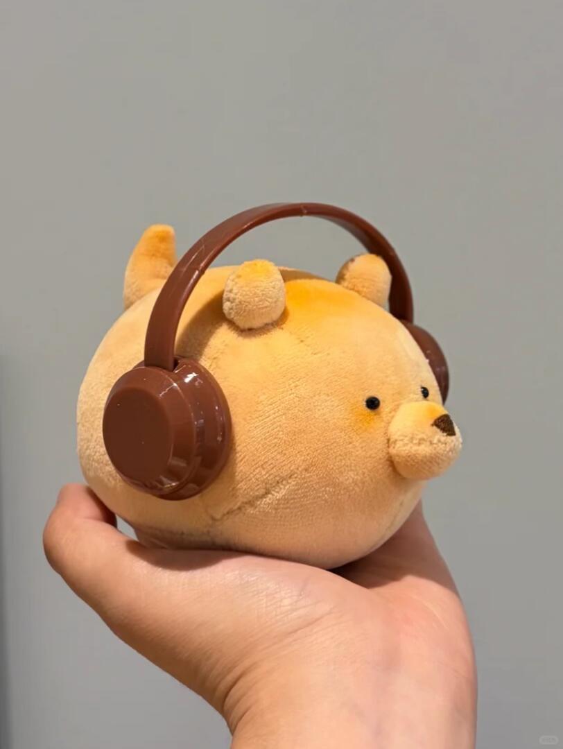 Plush toy with headphones held in a hand against a gray background
