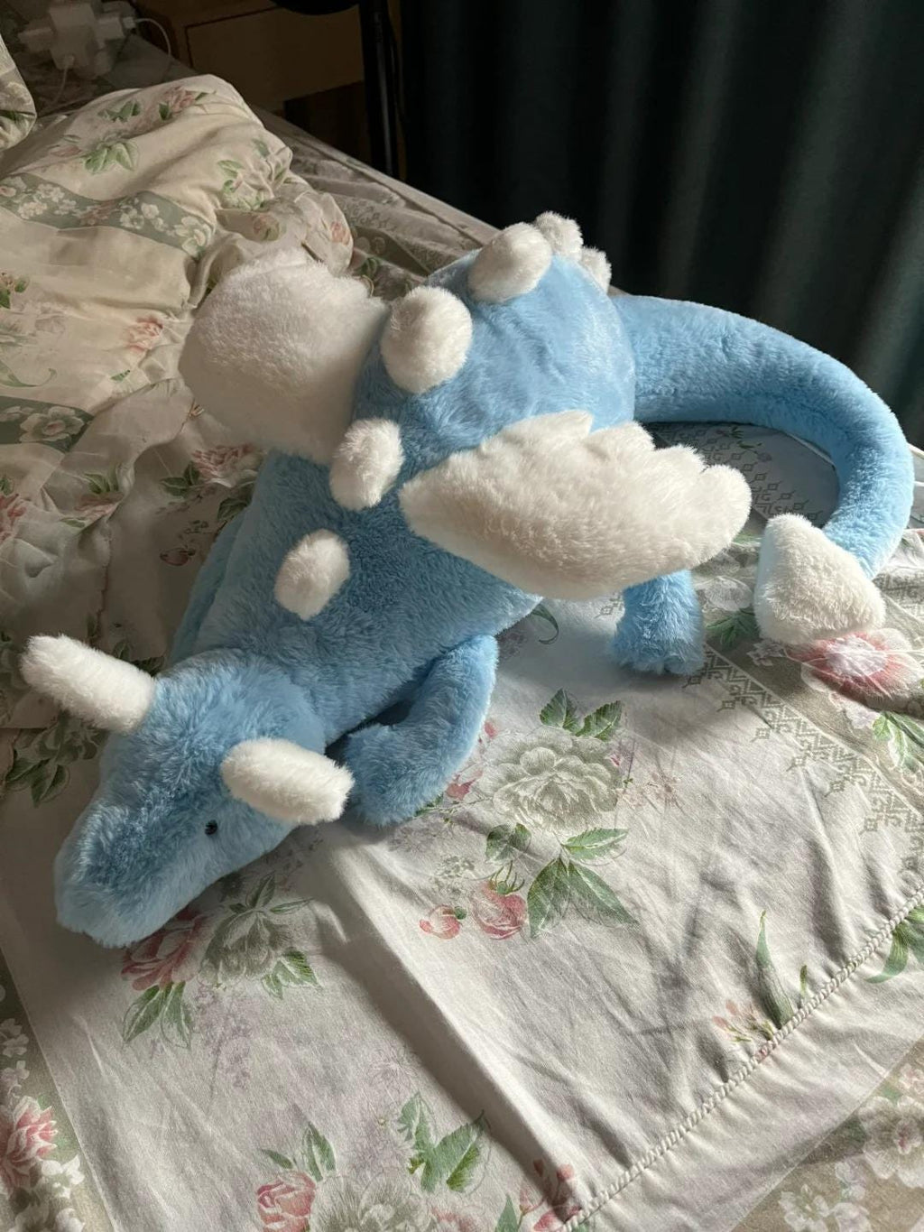 Blue dragon plush toy with white accents on a floral-patterned surface