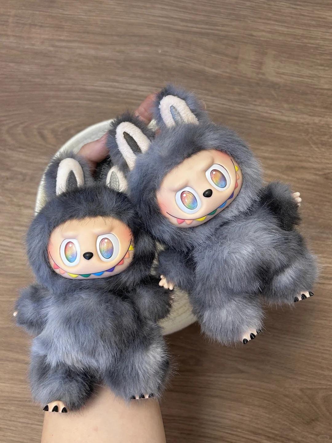 Pair of fuzzy special hidden labubu with cartoon face design on a wooden floor.