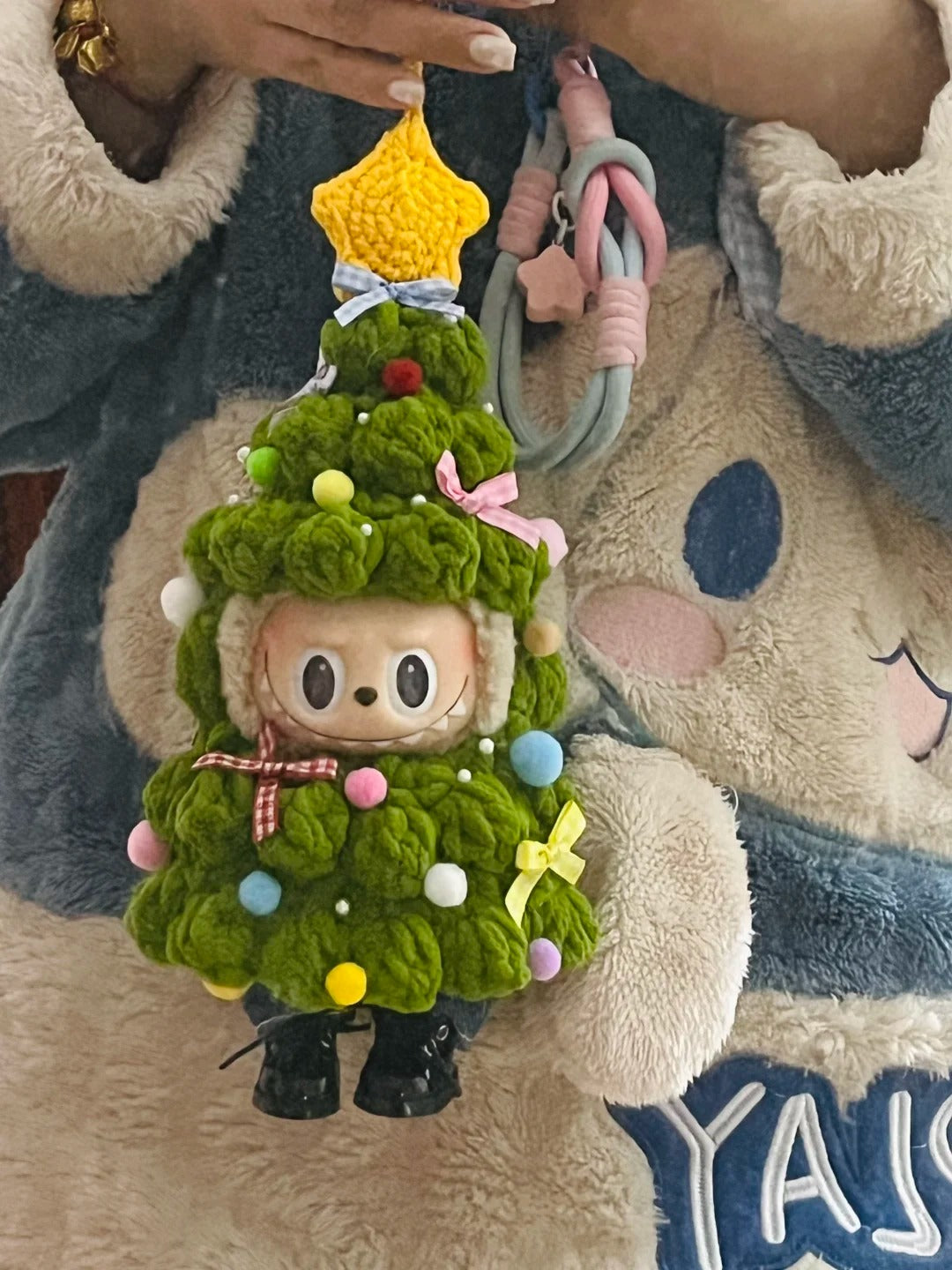 Bag charm resembling a Christmas tree with a Labubu inside, held by a hand.