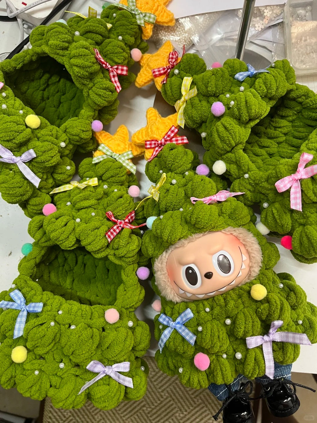 Green knitted wreath looks like christmas tree with colorful decorations and a  labubu plush toy inside.