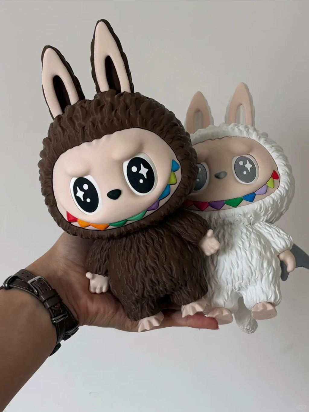 3D Printing file for Labubu, Two plush toys, one brown and one white, held in a hand against a plain background.
