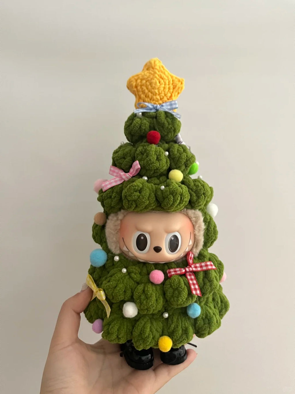 Labubu dressing a Christmas tree outfit with colorful decorations held by a hand against a plain background