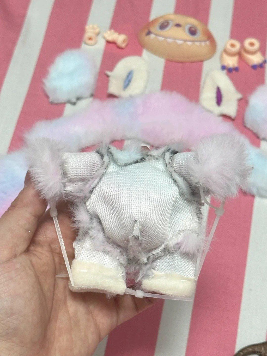 How to sew a labubu: Small white plush toy with pink hair bow held by a hand against a colorful background.
