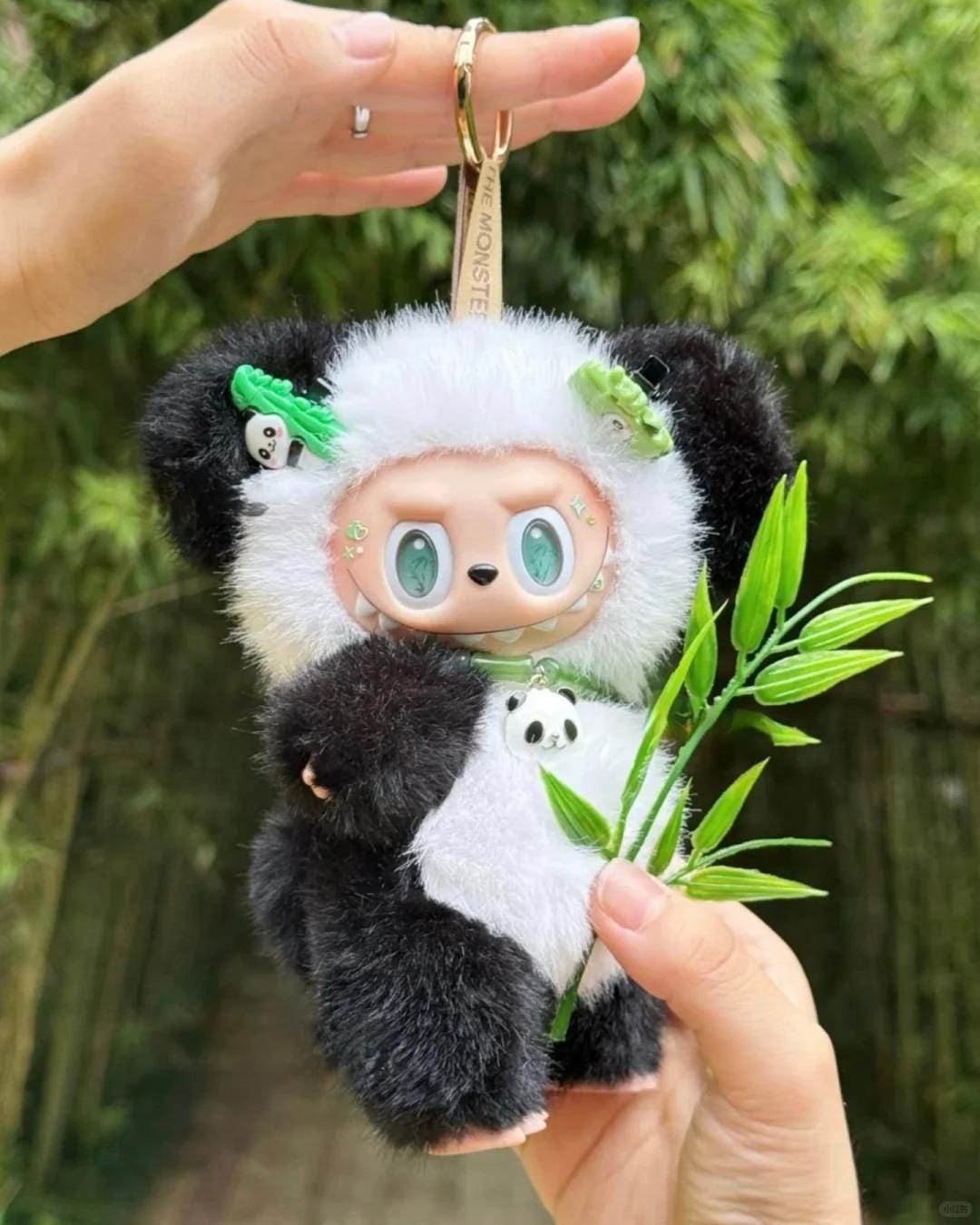 Plush labubu keychain with panda design held by a hand against a blurred green background