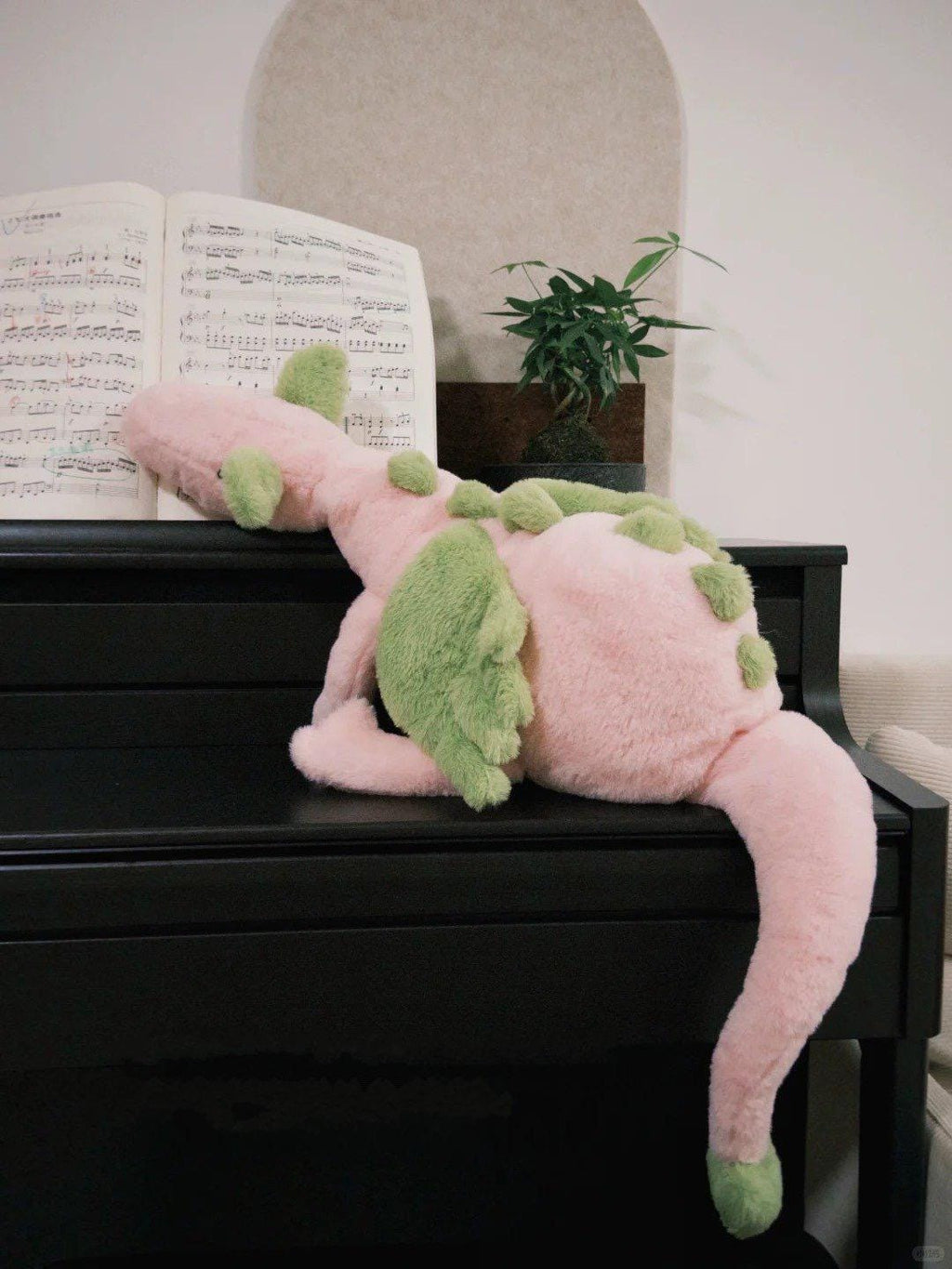Plush pink dragon toy on a piano with sheet music in the background