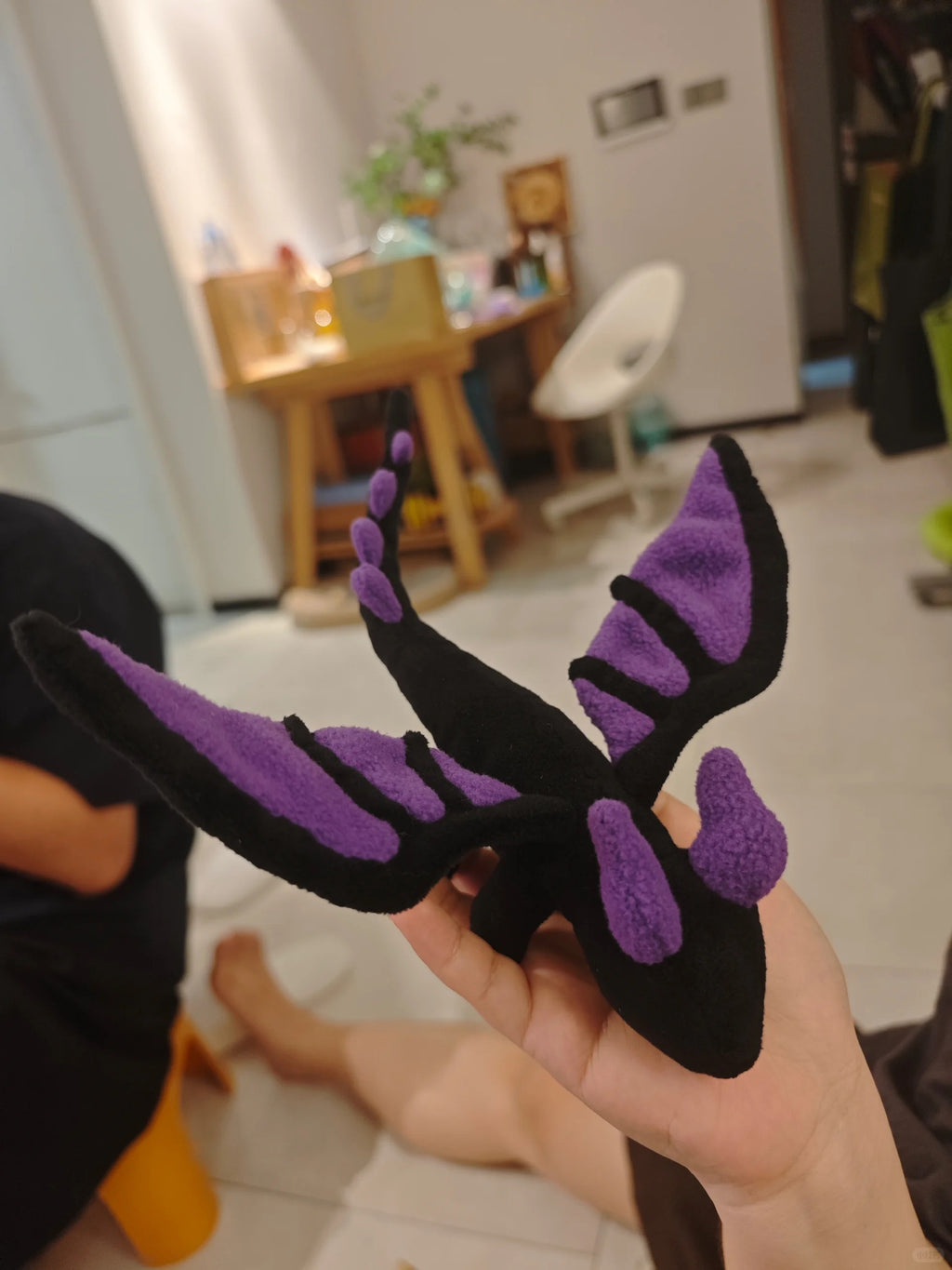 Black and purple dragon-shaped toy plushie held in a hand with a blurred indoor background