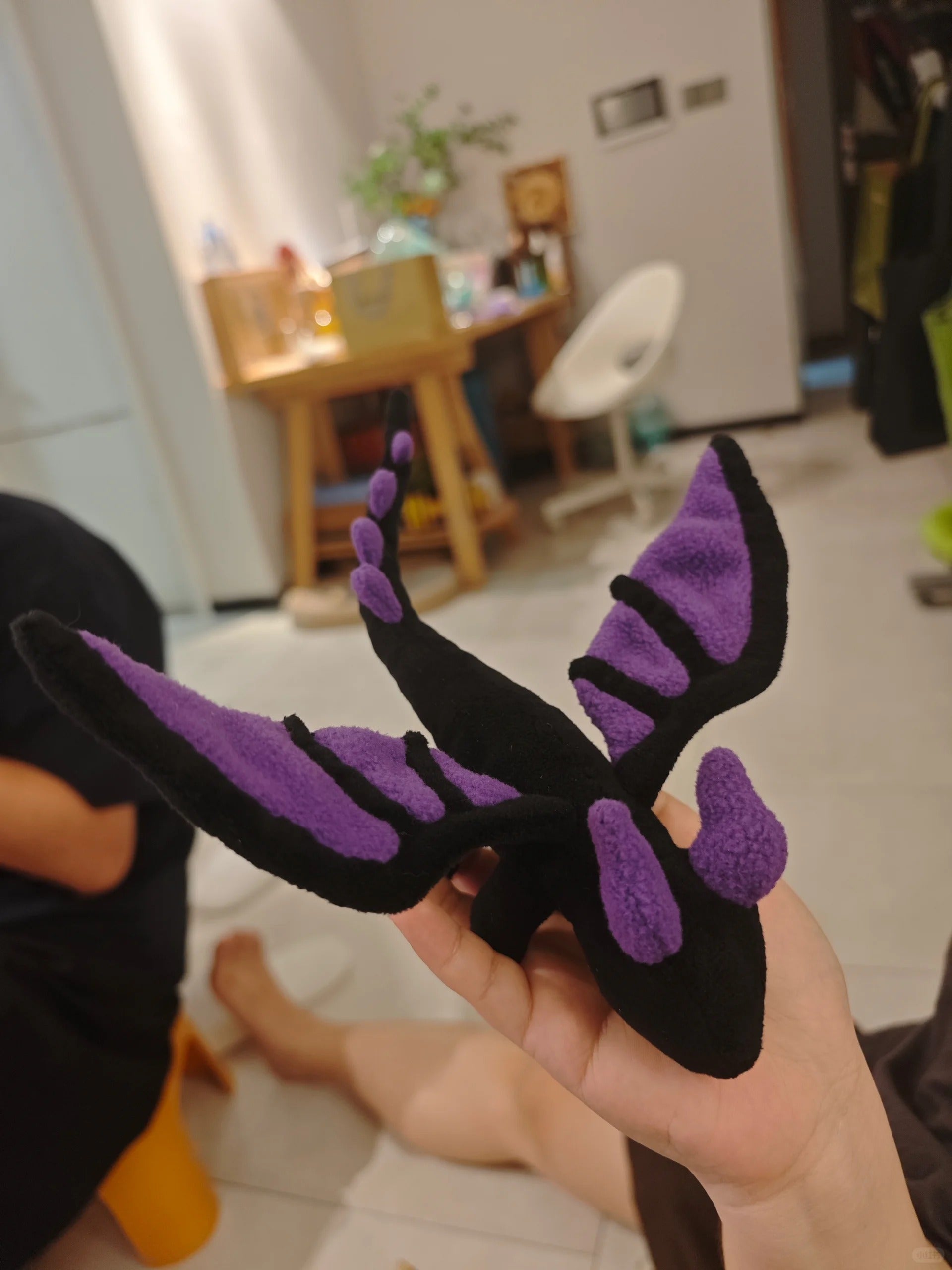 Black and purple dragon-shaped toy plushie held in a hand with a blurred indoor background