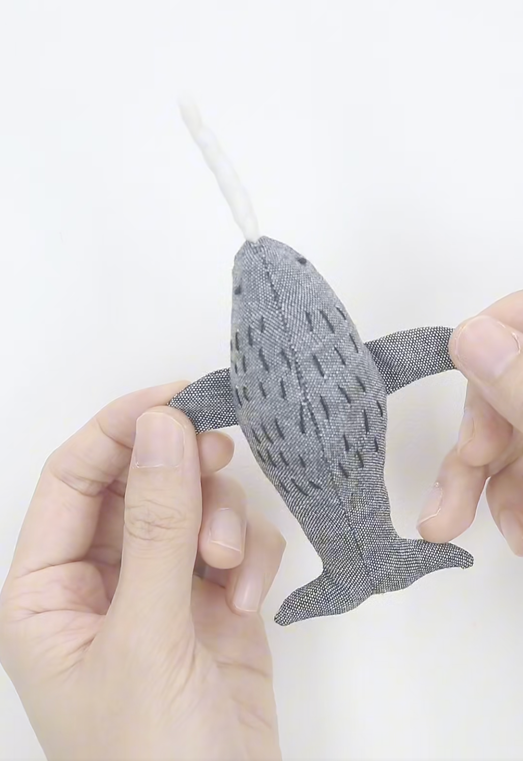 Gray whale-shaped object held by a hand on a white background
