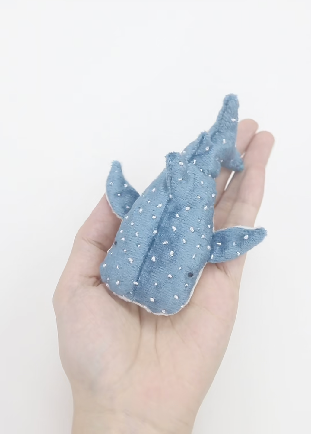 Hand holding a small blue shark plush toy with white polka dots on a white background