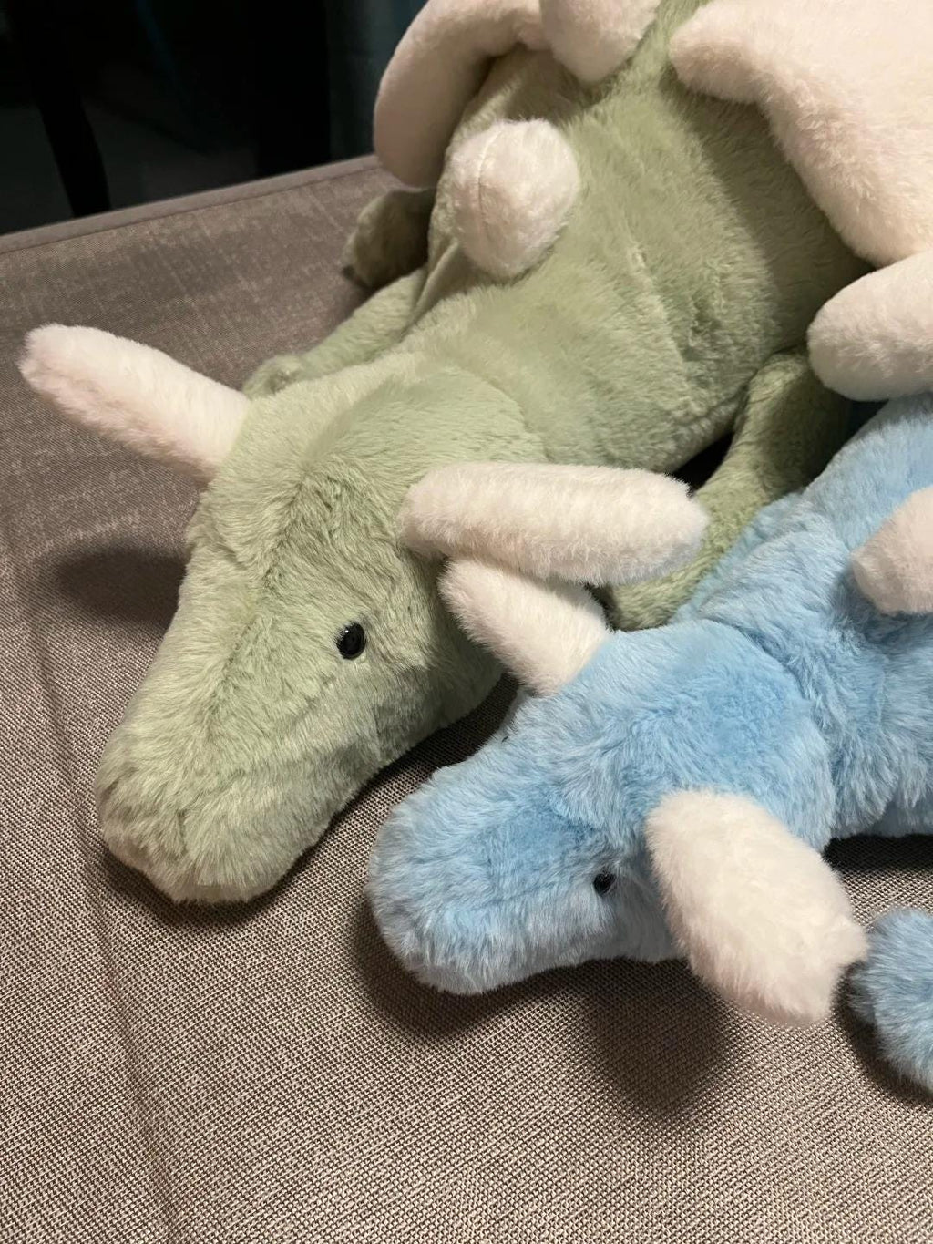 Two sky dragon plush toys, one green and one blue, on a textured surface.