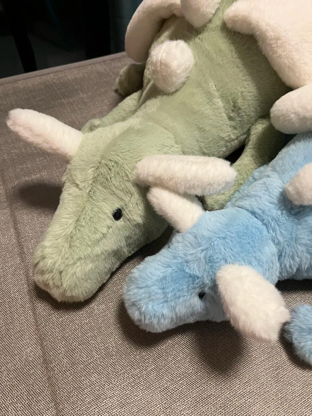 Two sky dragon plush toys, one green and one blue, on a textured surface.