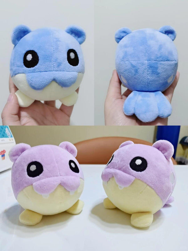 Two pokemon Spheal plush toys, one blue and one purple, held by a hand against a white background.