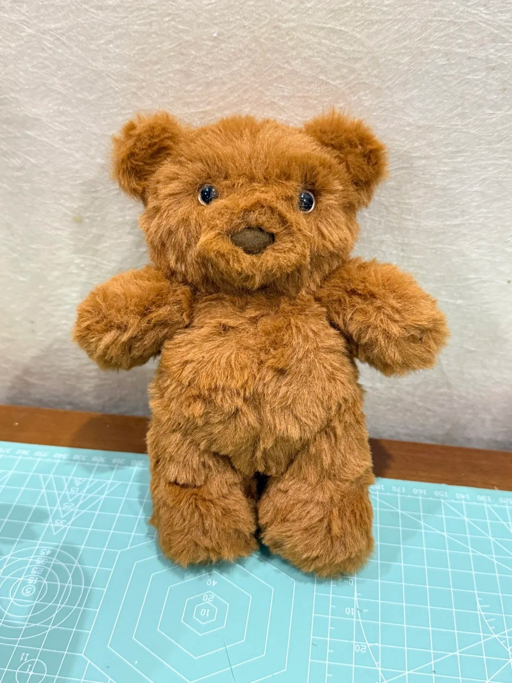 Brown teddy bear on a cutting mat with a textured wall background