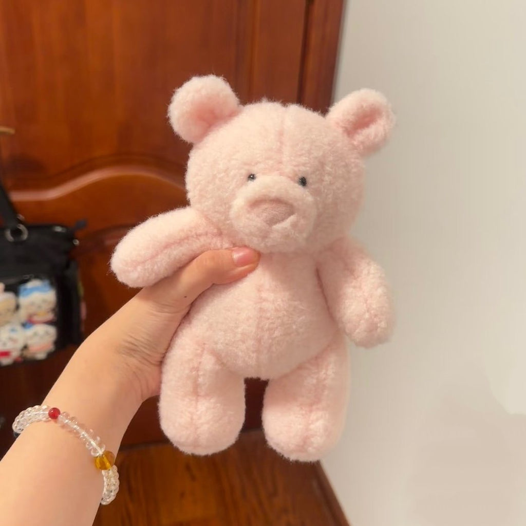 Pink teddy bear held by a hand with a bracelet against a wooden background