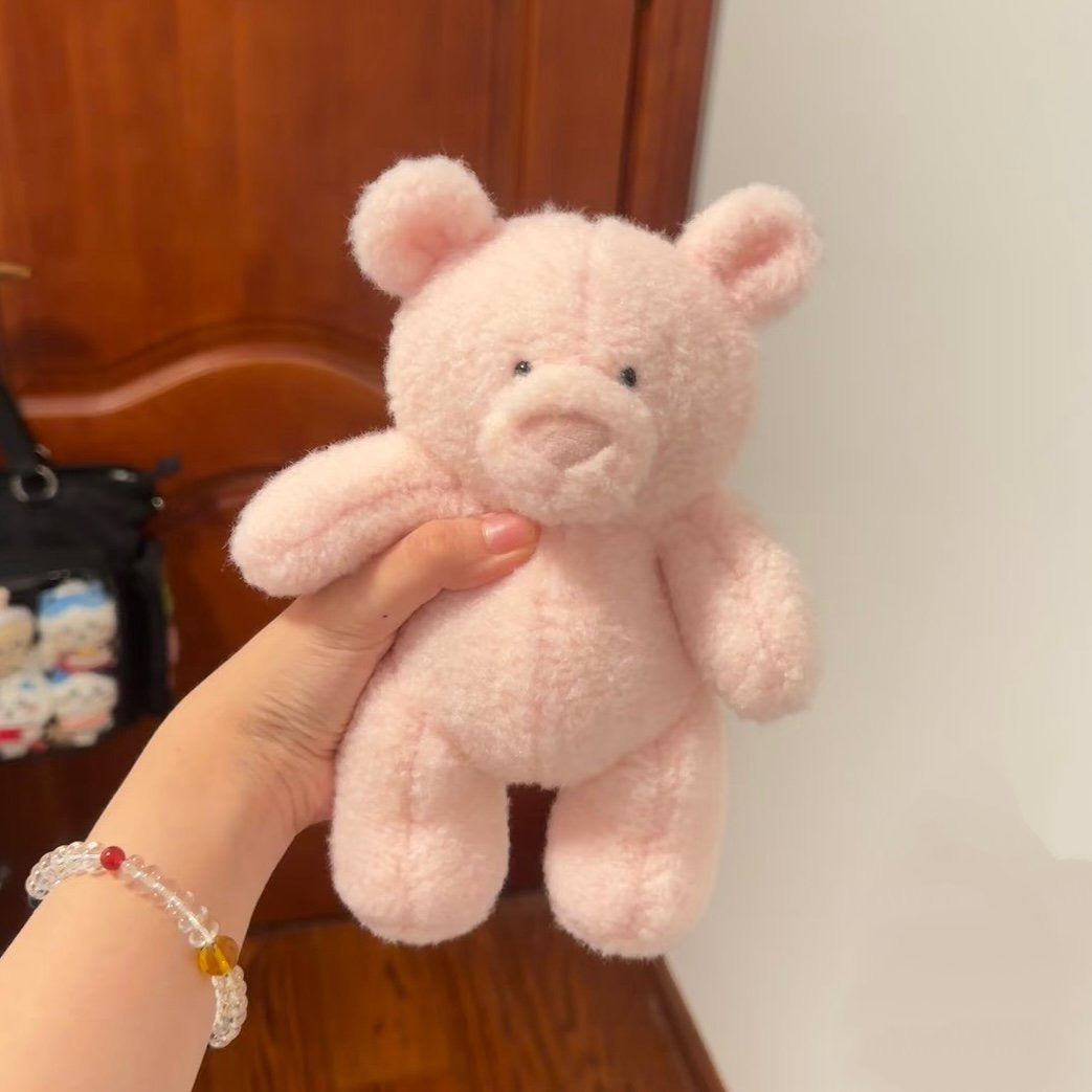Pink teddy bear held by a hand with a bracelet against a wooden background