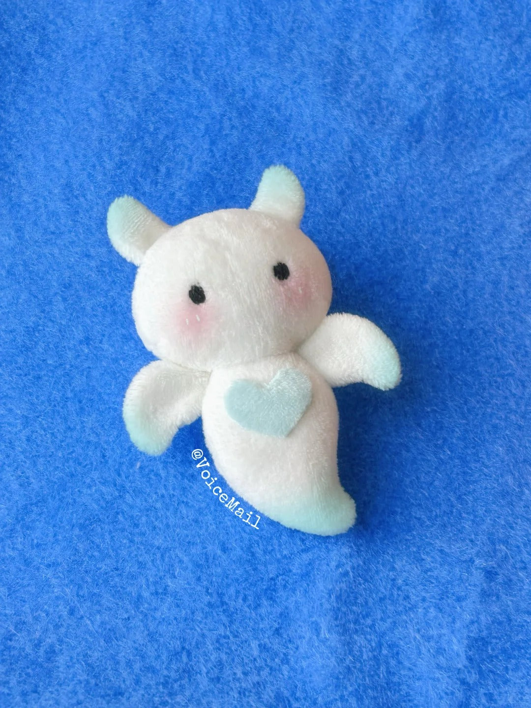 White angel bat plush with mint heart and soft wings on blue background