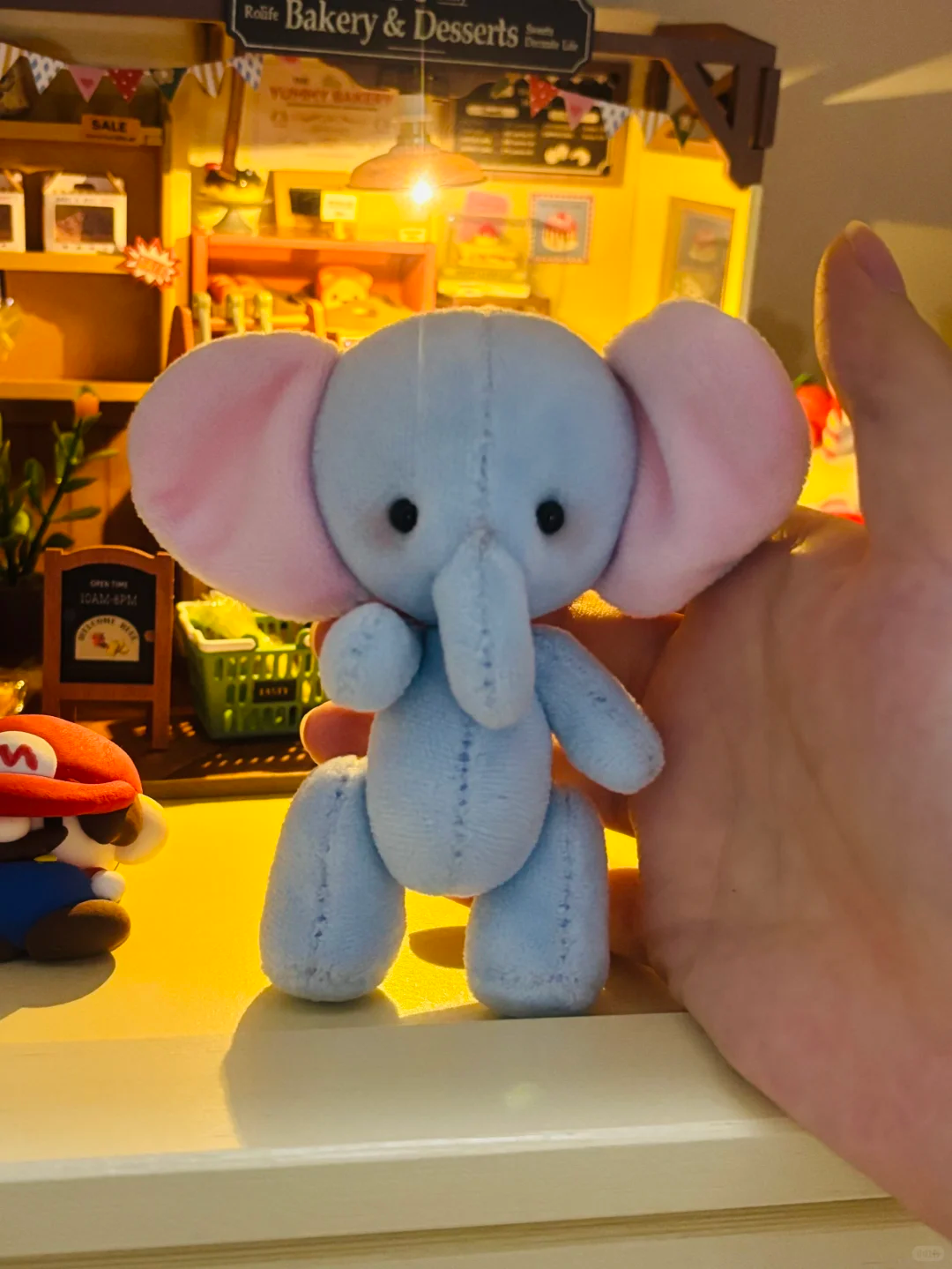 Small light blue elephant soft toy shown beside a hand for scale in warm light