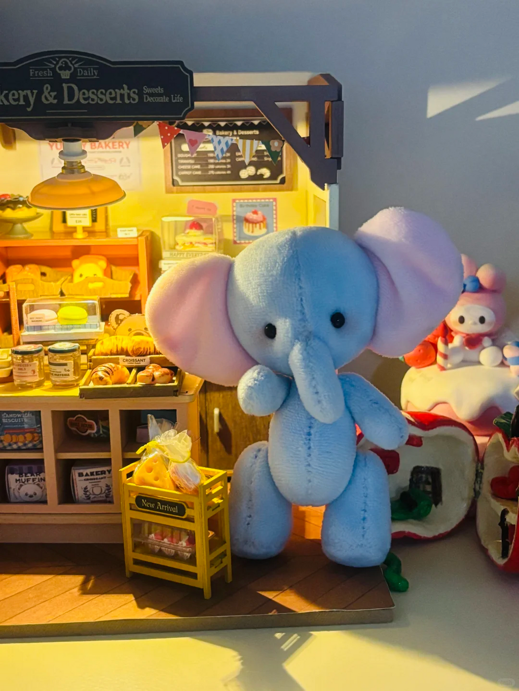 Light blue handmade elephant plush displayed beside a miniature bakery scene
