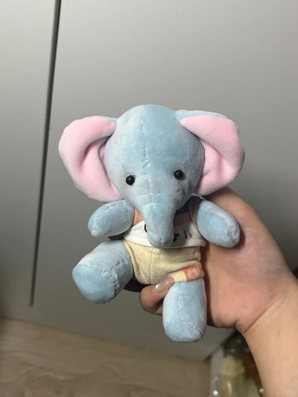 Handheld light blue elephant plush wearing a miniature cream outfit