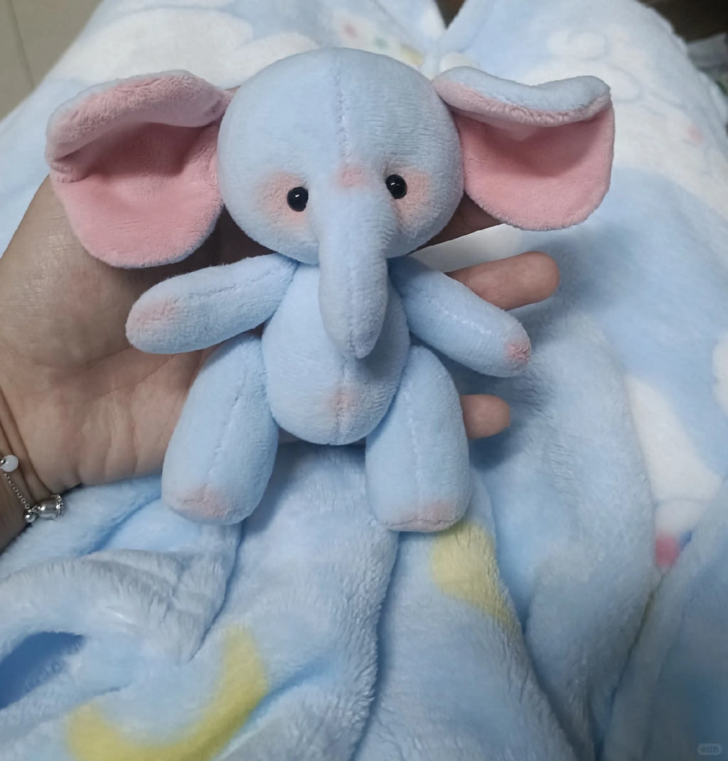 Close-up of a palm-sized blue elephant plush with wide pink inner ears
