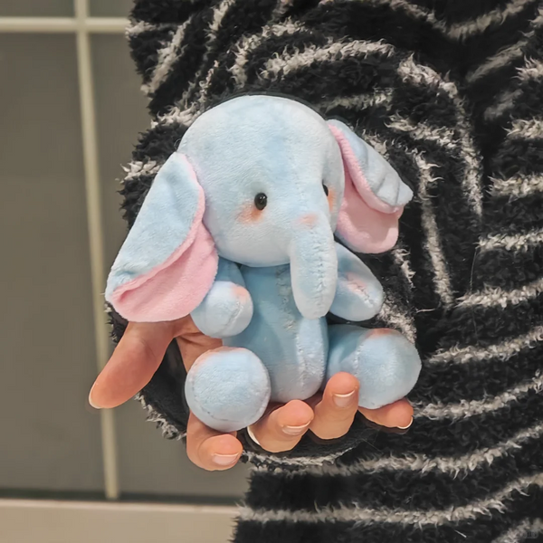Front view of a light blue elephant plush with pink inner ears held in one hand