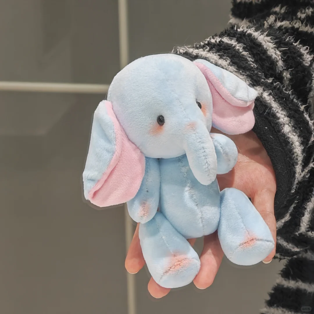 Side view of a handmade light blue elephant soft toy with pink ear details