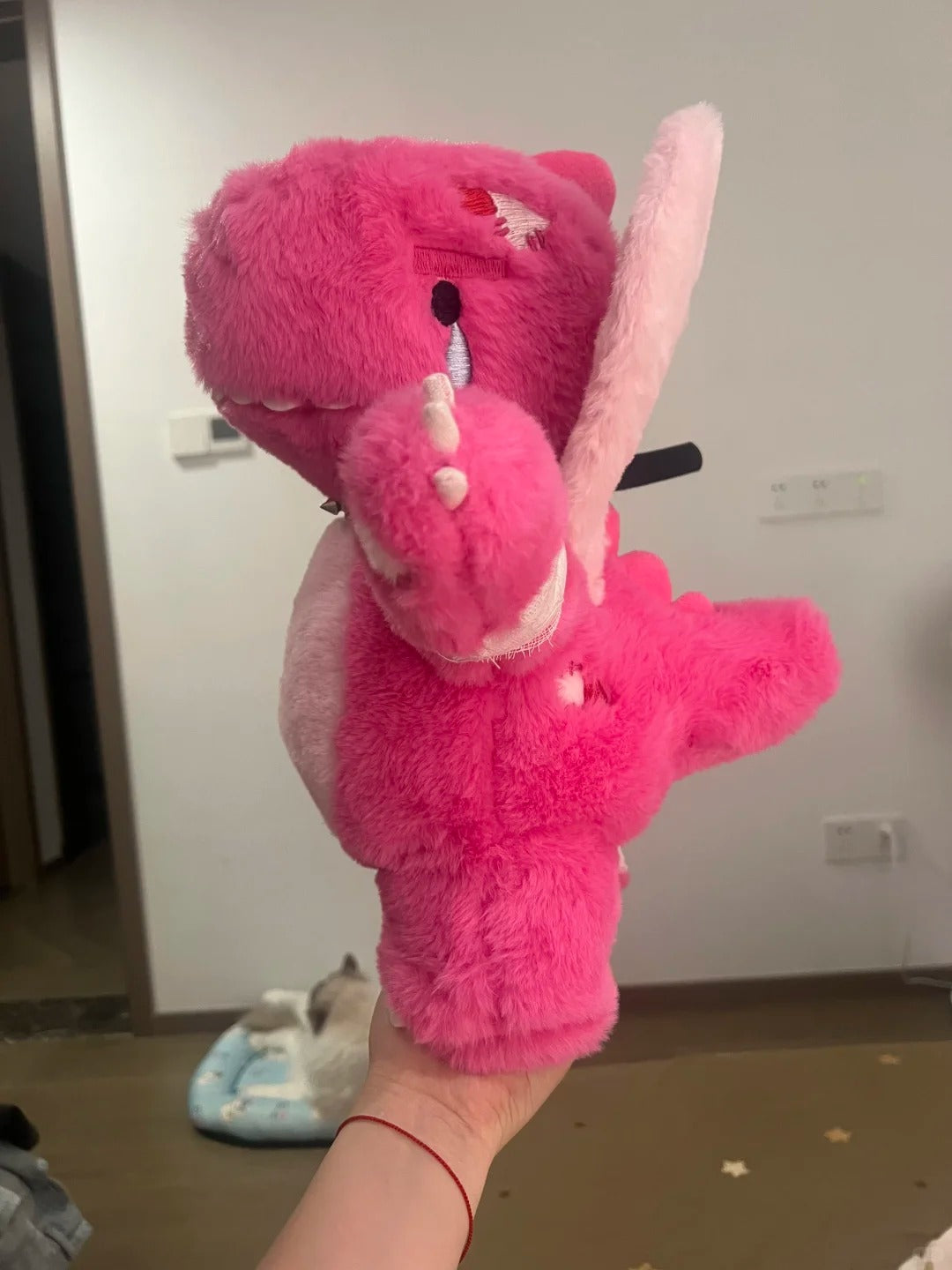 Full-body view of a pink Boltusk dragon plush held up to show its legs, tusks, and tail
