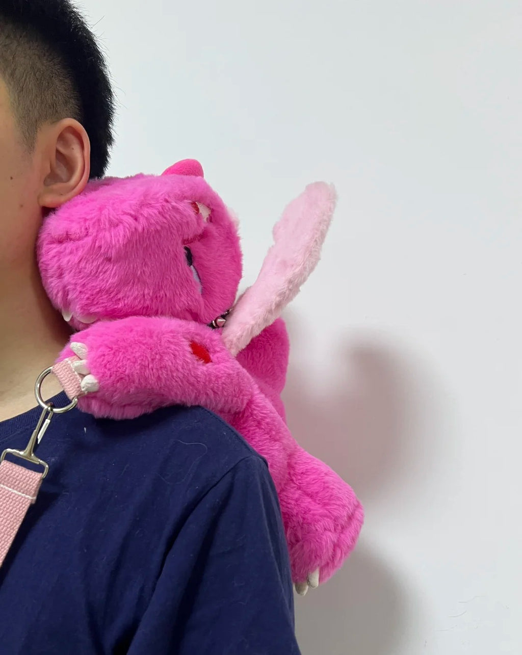 Pink Boltusk dragon plush resting over a shoulder with long tusks and carrying strap