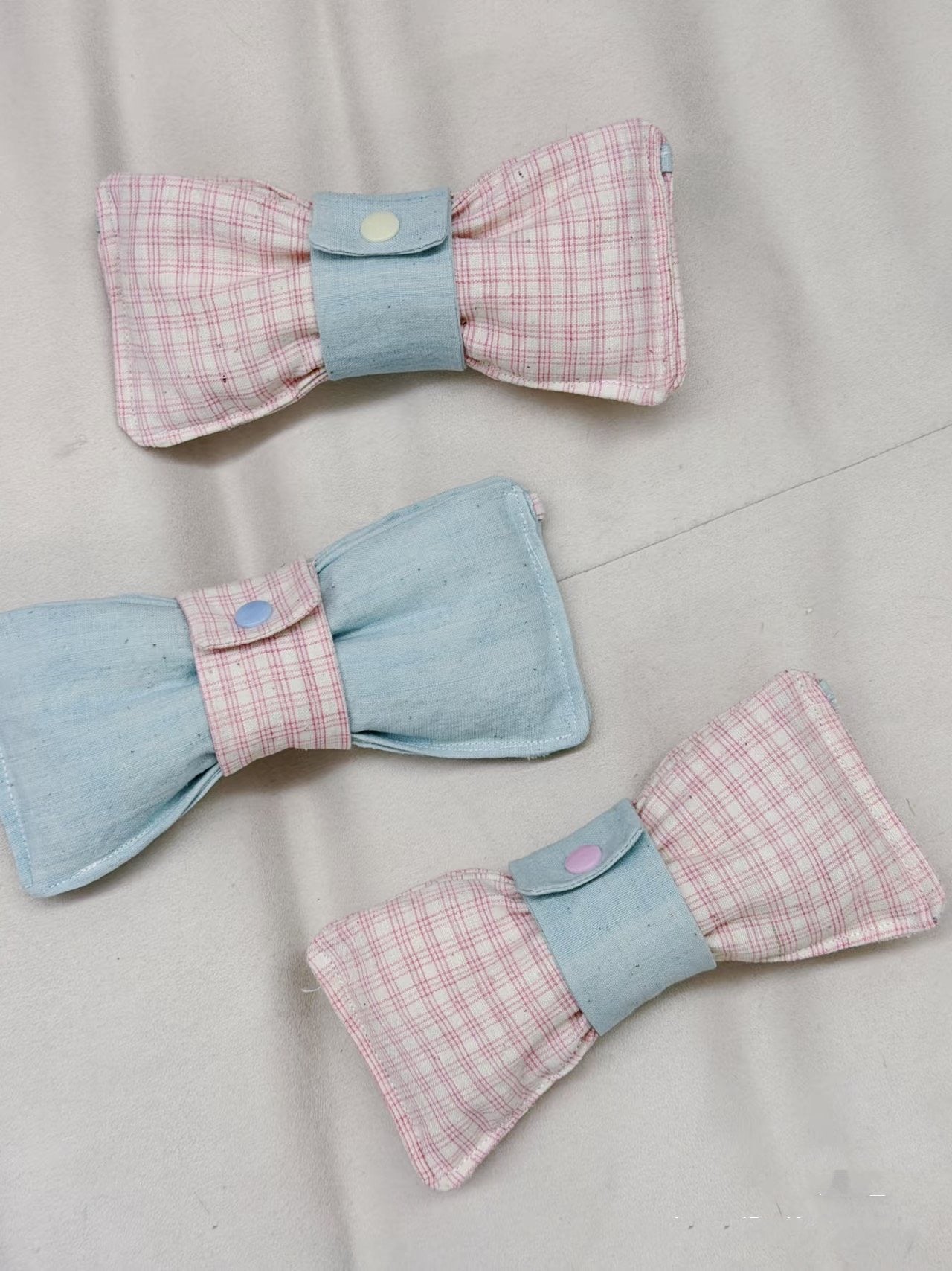 Three fabric bows with pink and blue checkered patterns on a light gray background