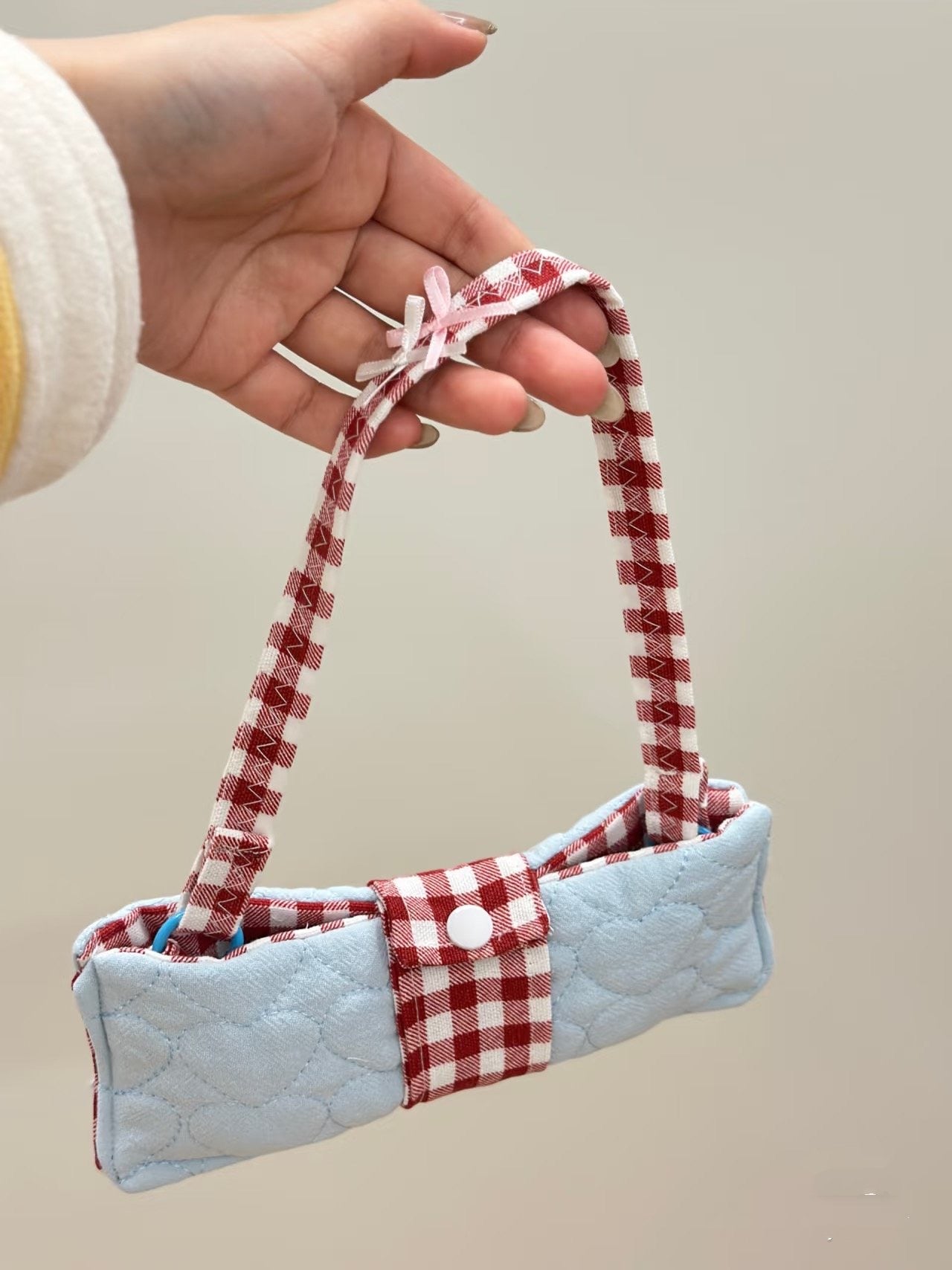 Small quilted bag with red and white checkered handle held by a hand against a neutral background