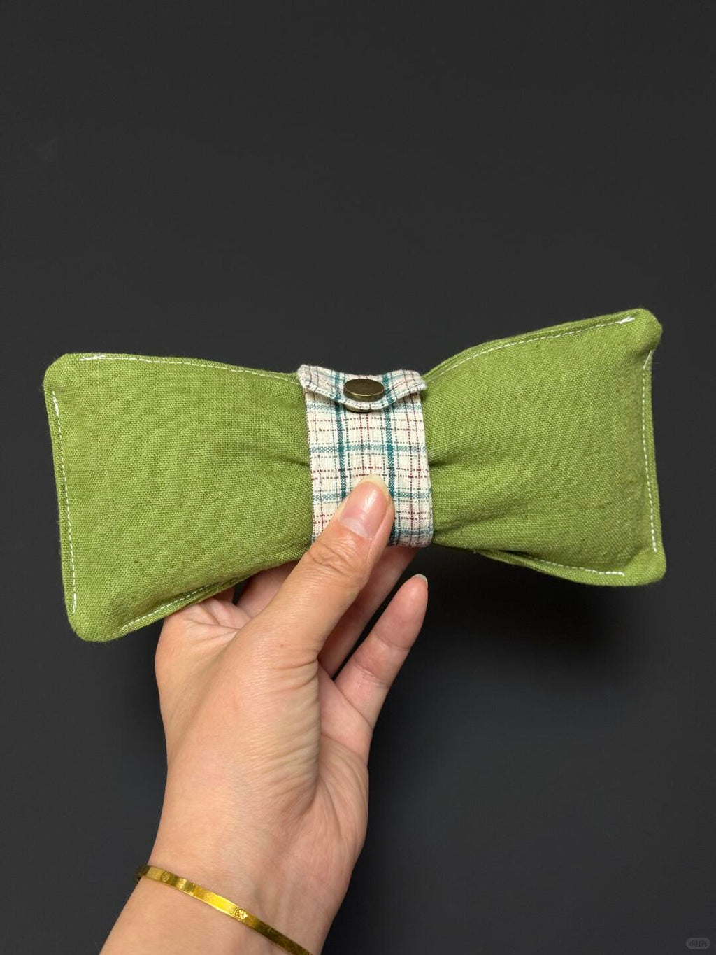 Green fabric bow tie held by a hand against a dark background