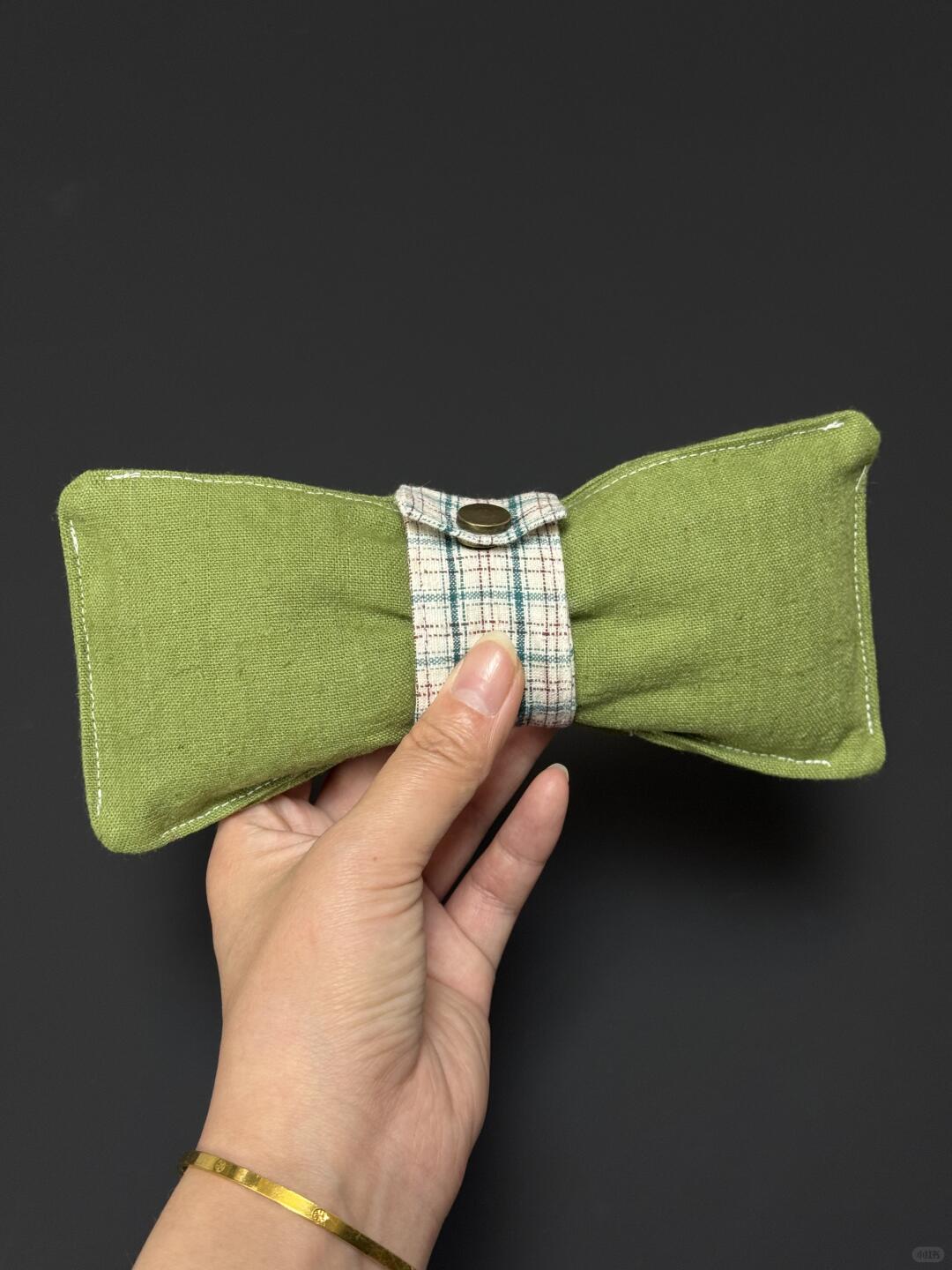 Green fabric bow tie held by a hand against a dark background