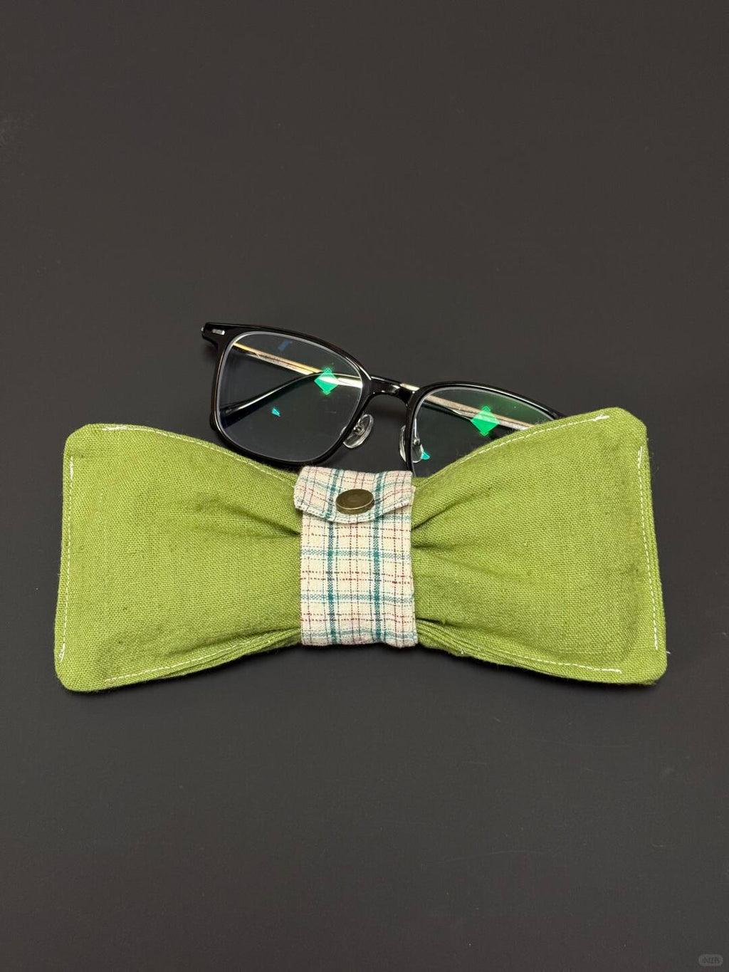 Green bow tie glasses case with a pair of glasses on a dark background