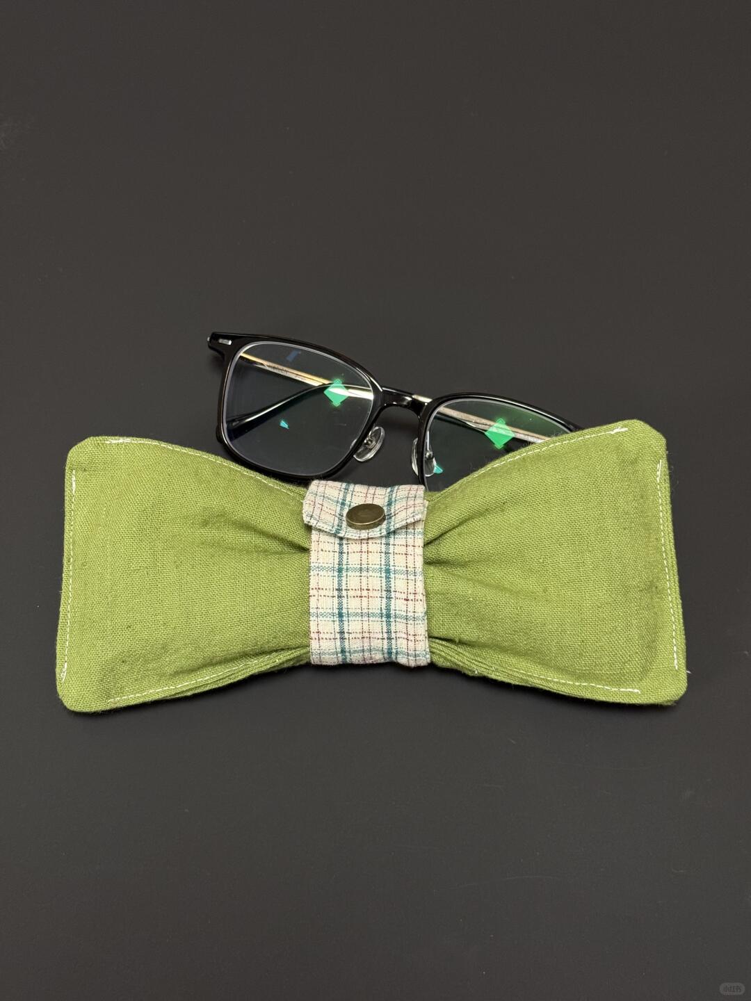 Green bow tie glasses case with a pair of glasses on a dark background