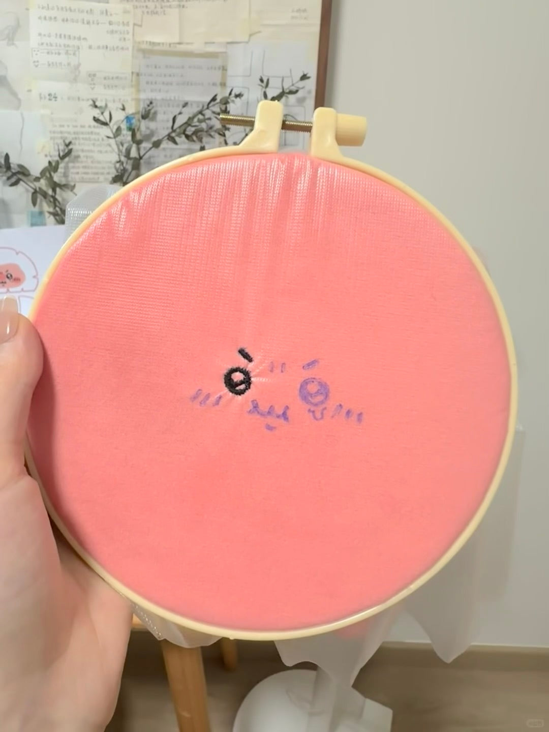 Embroidery hoop showing the facial embroidery process for a pink angry plush