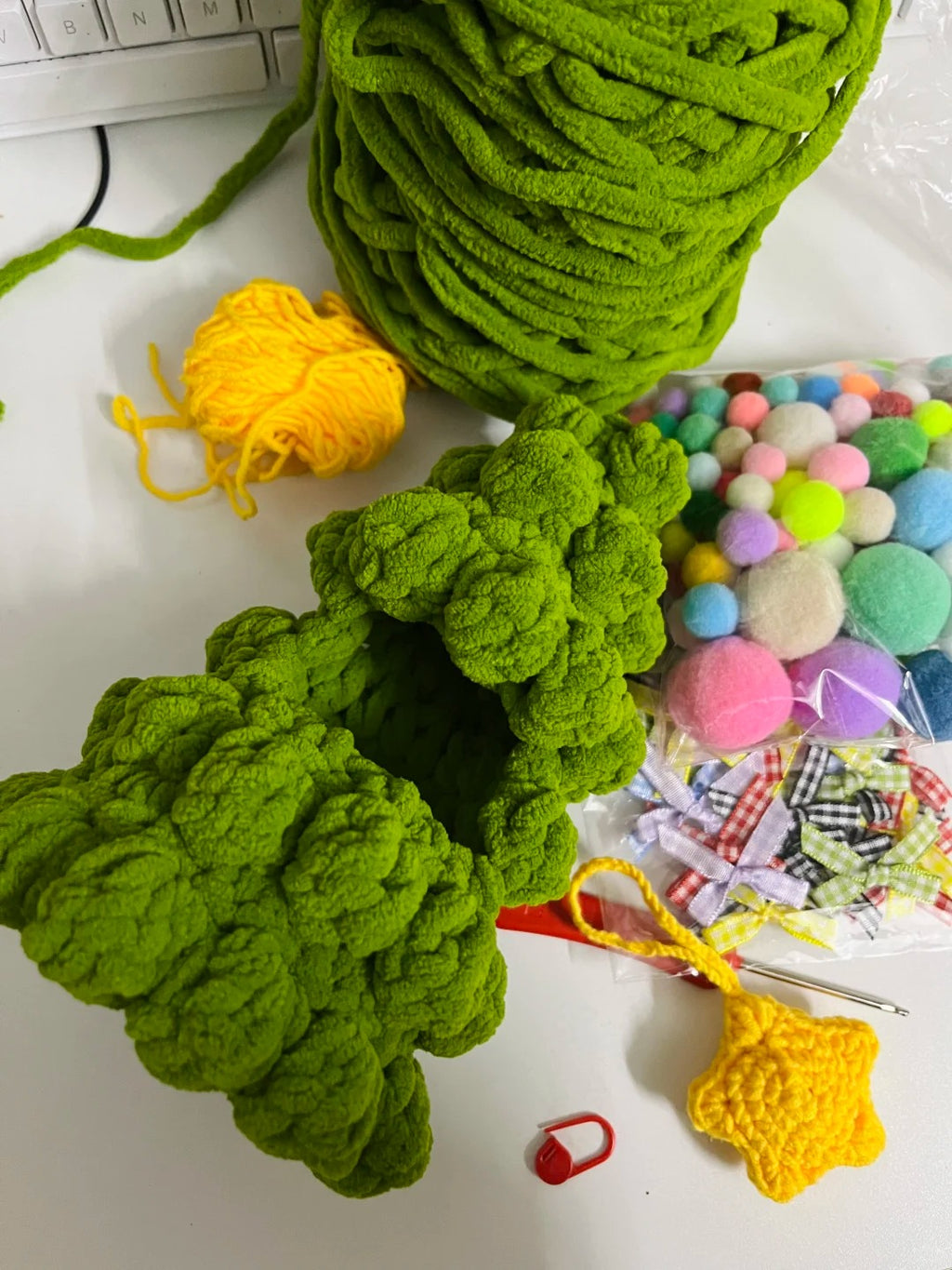 A Christmas tree crochet by Green yarn balls and colorful pom-poms on a white surface 