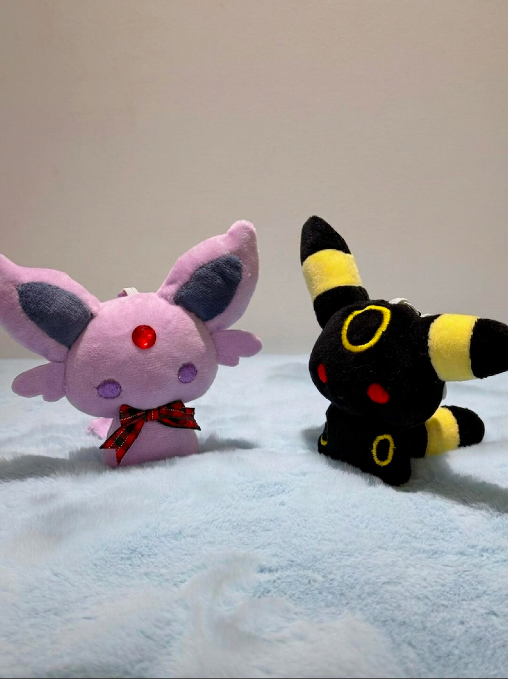 eevee evolutions plush toys, one pink with large ears and the other black and yellow, on a light blue blanket.