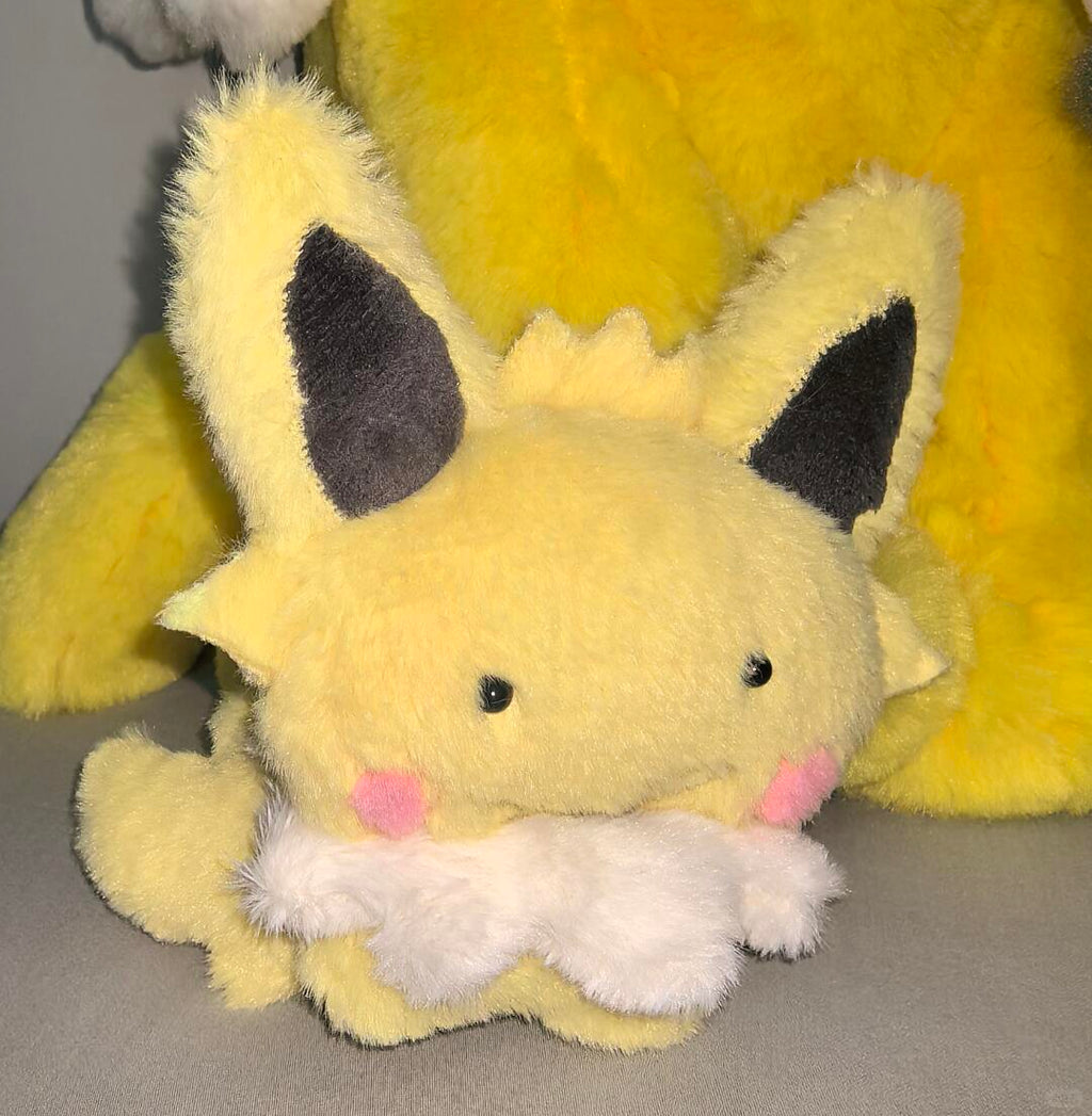 Handmade yellow Eeveelution plush sewn from the pattern, photographed with large plush toys in the background